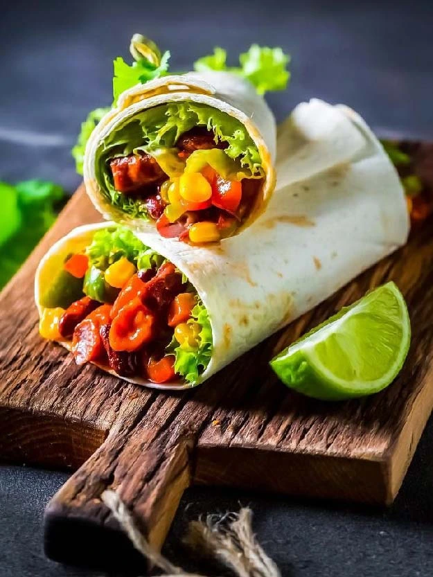 a burrito with vegetables and lettuce on a cutting board